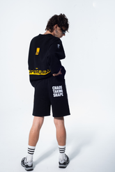 Model in the Haresquare Superhuman black sweatshirt with yellow print, styled with Haresquare black shorts – unisex luxury streetwear from Ireland.